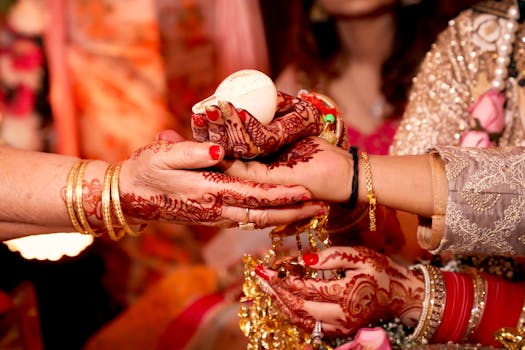 Close-up of hands with henna tattoos exchanging an object during a cultural ceremony.