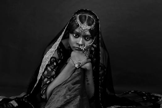 Striking black and white portrait of a woman adorned with traditional Indian jewelry, expressing deep emotion.